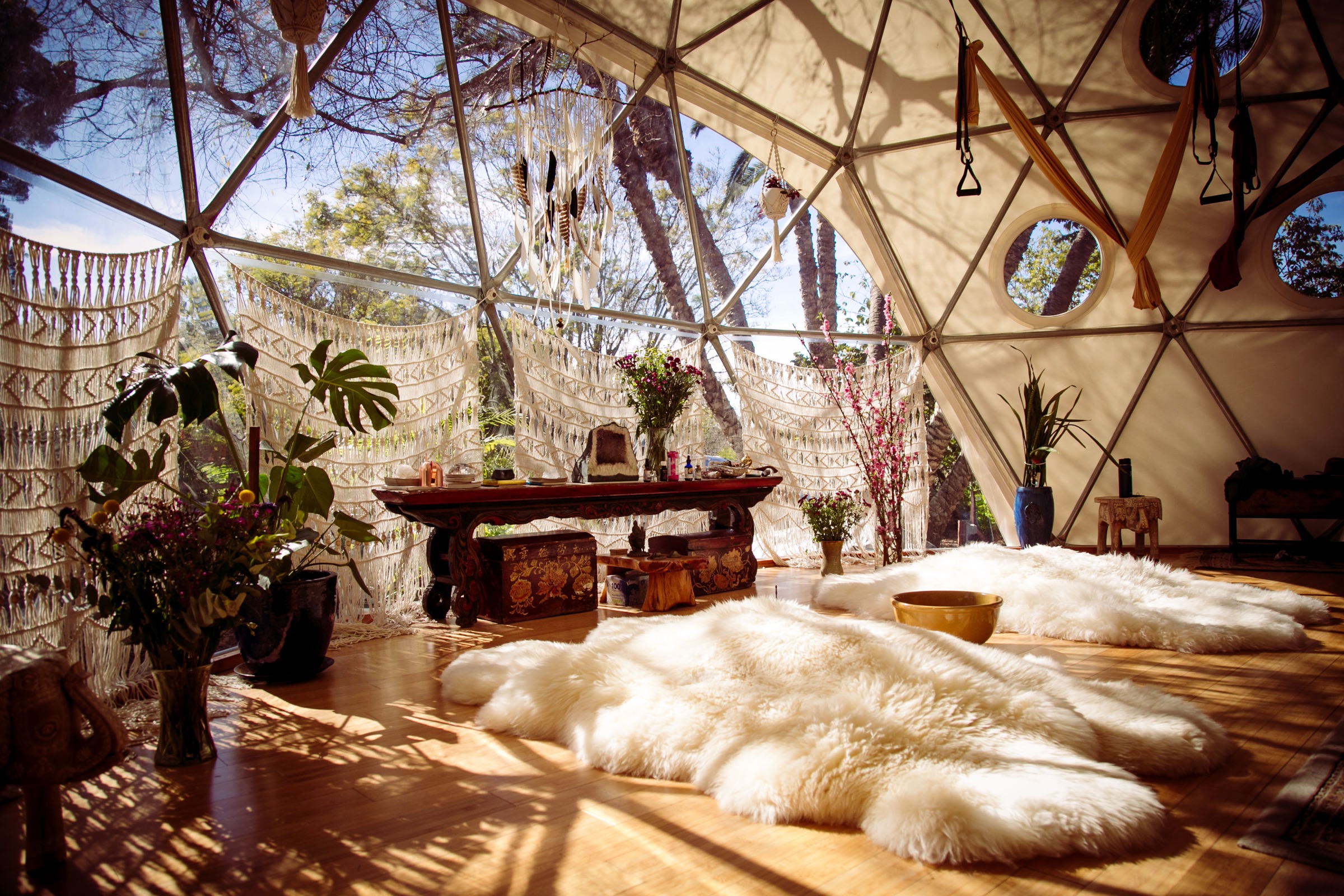 A wide view of the sunlit Aum Dome interior with sheepskins spread across the wood floor