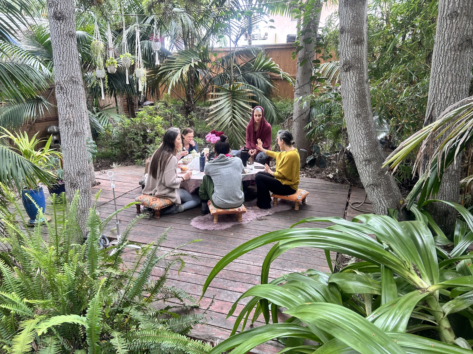 A group gathered around a low table on the wooden deck outside the Aum Dome, surrounded by tropical planting